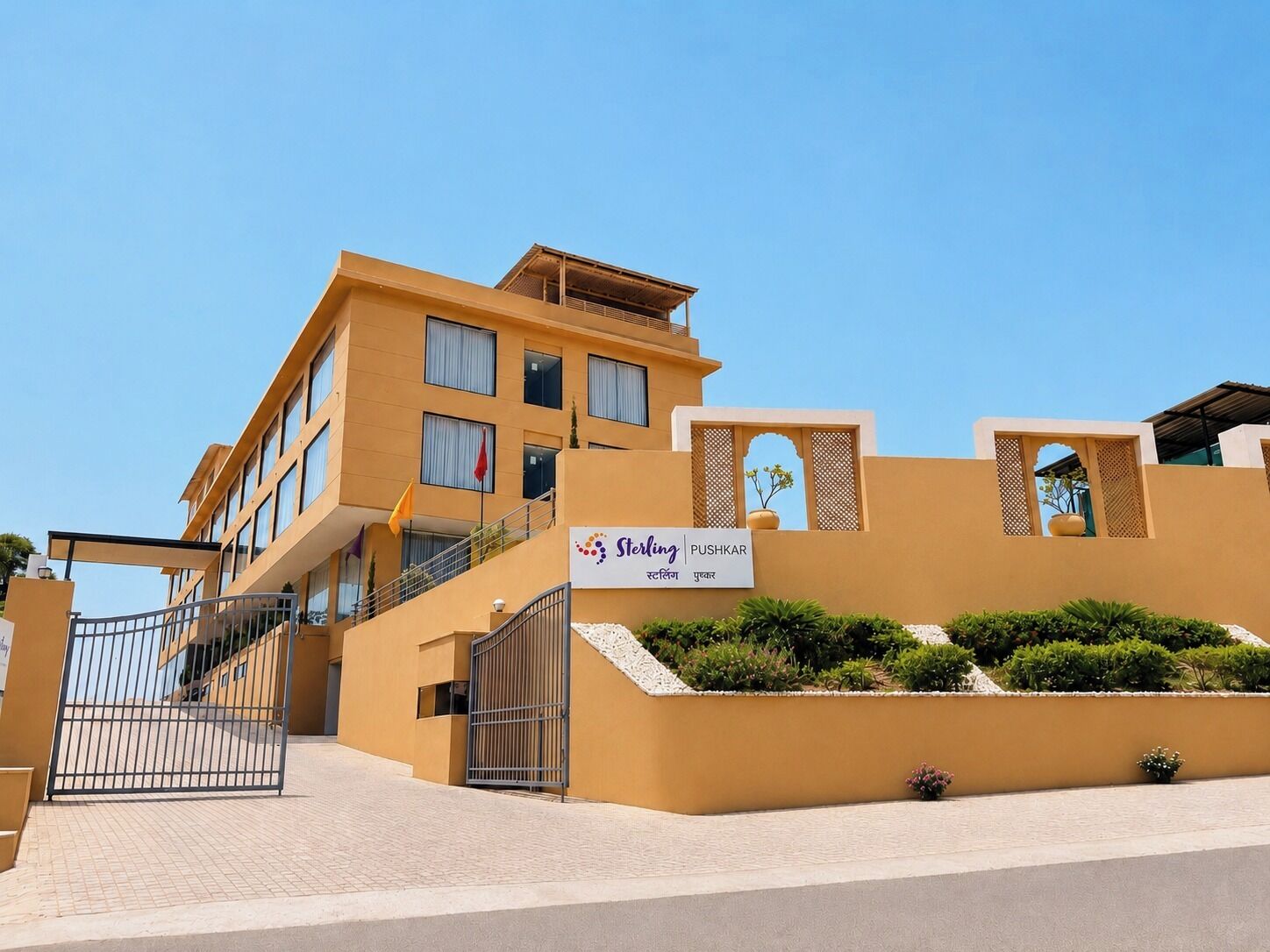 A hotel with a yellow facade, a gated entrance, and a signboard with the name 'Sterling PUSHKAR'.