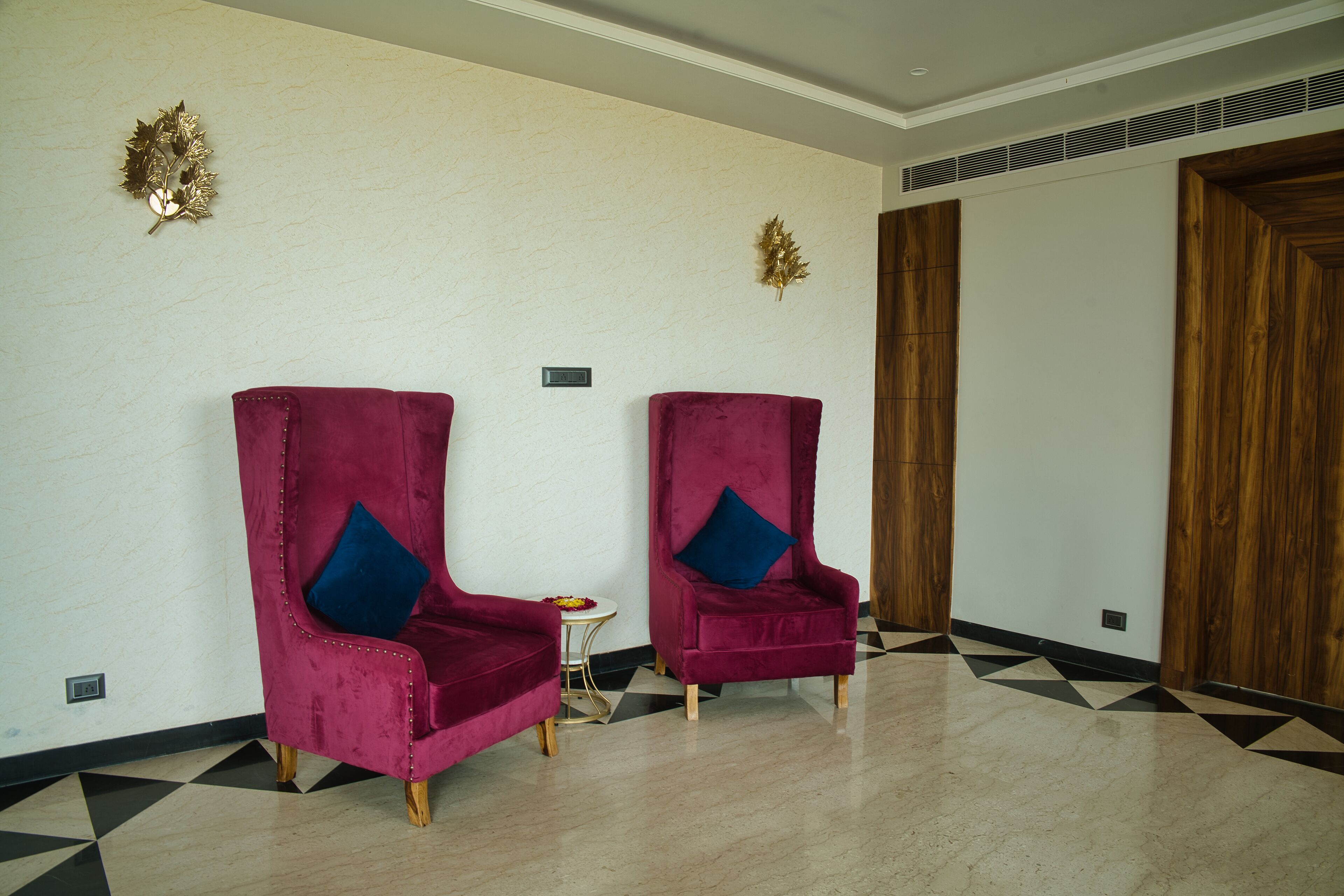 Two plush red chairs with blue cushions, a small round table with a flower, and a geometric patterned floor.