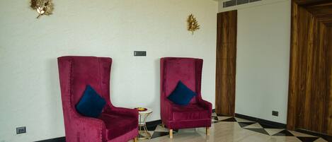 Two plush red chairs with blue cushions, a small round table with a flower, and a geometric patterned floor.
