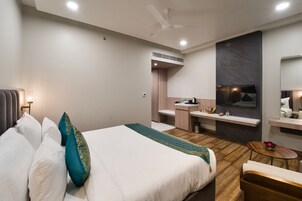A modern hotel room with a large bed, a small desk, a vanity, and a television.