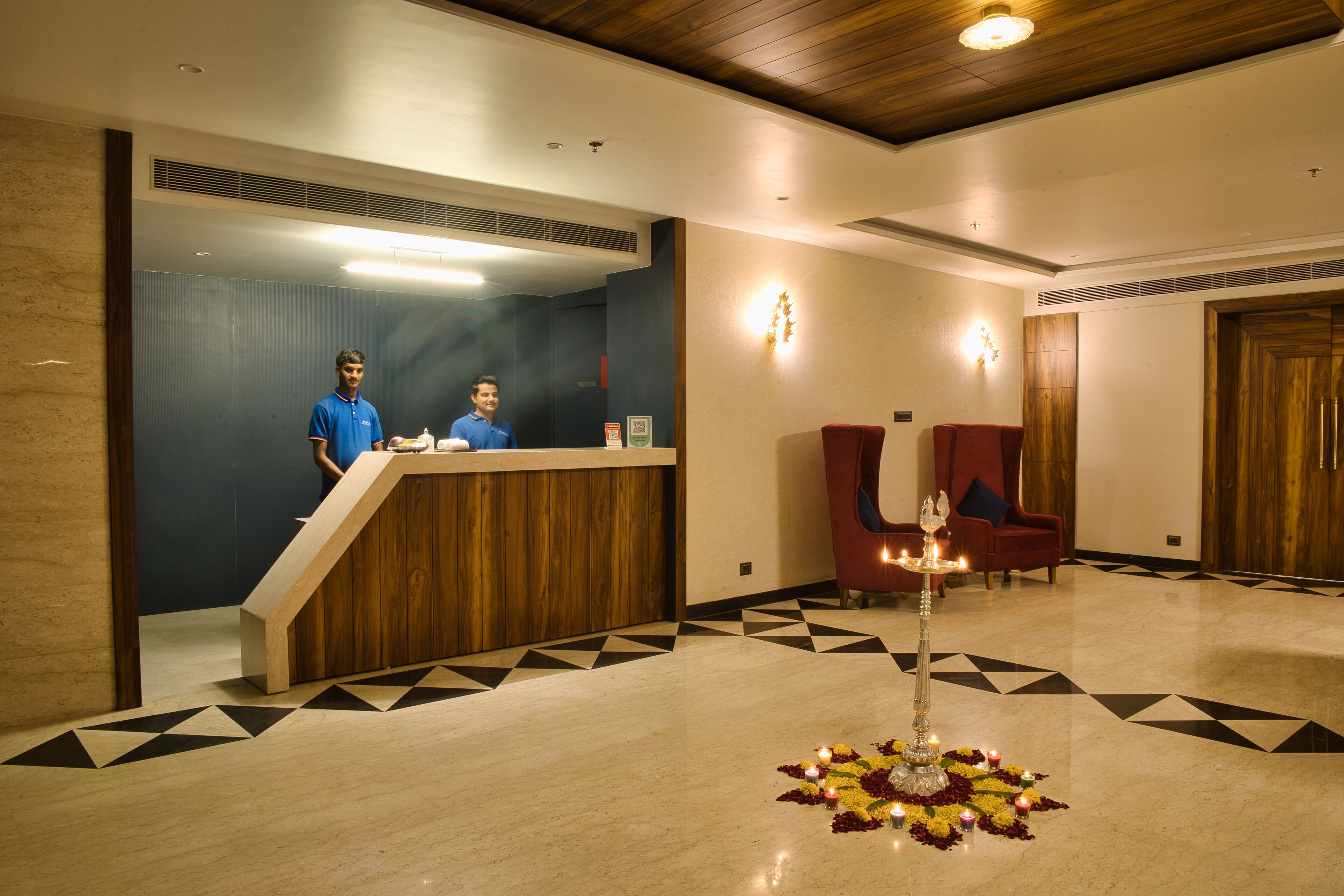 A hotel reception area with a wooden reception desk, a red armchair, and a decorative centerpiece with candles.