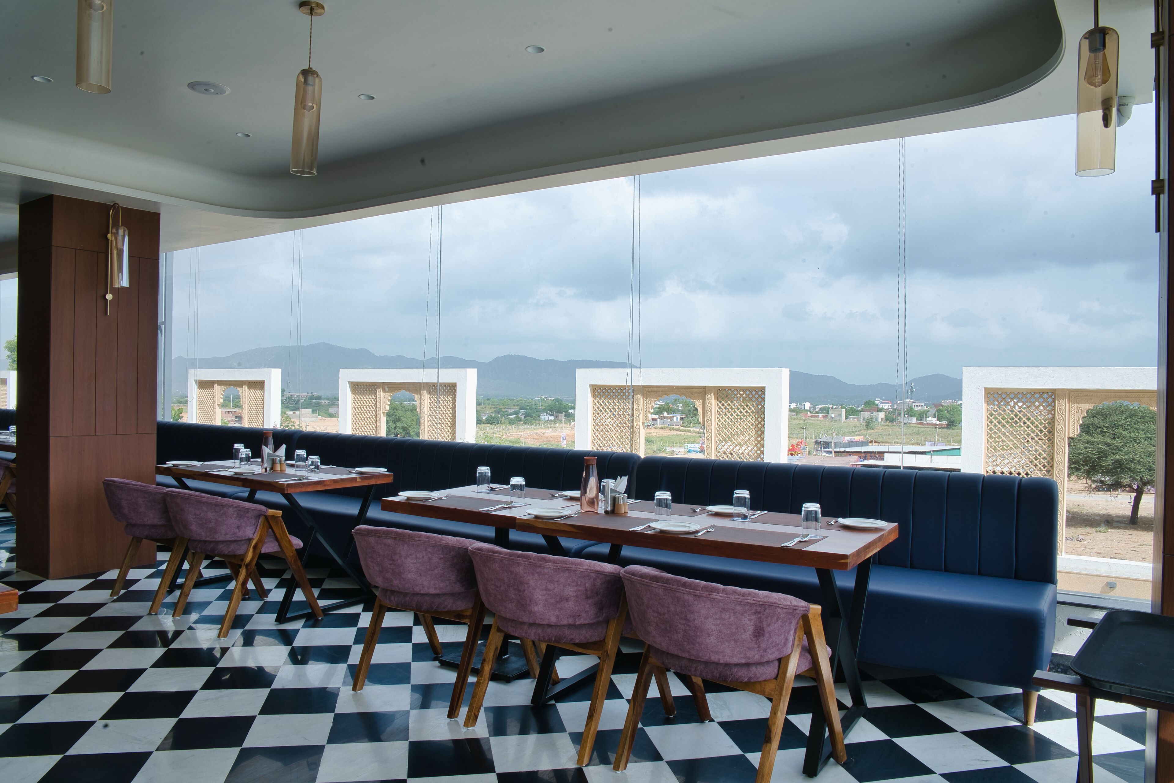 A restaurant with a checkered floor, wooden tables, purple chairs, and a large window overlooking a mountainous landscape.