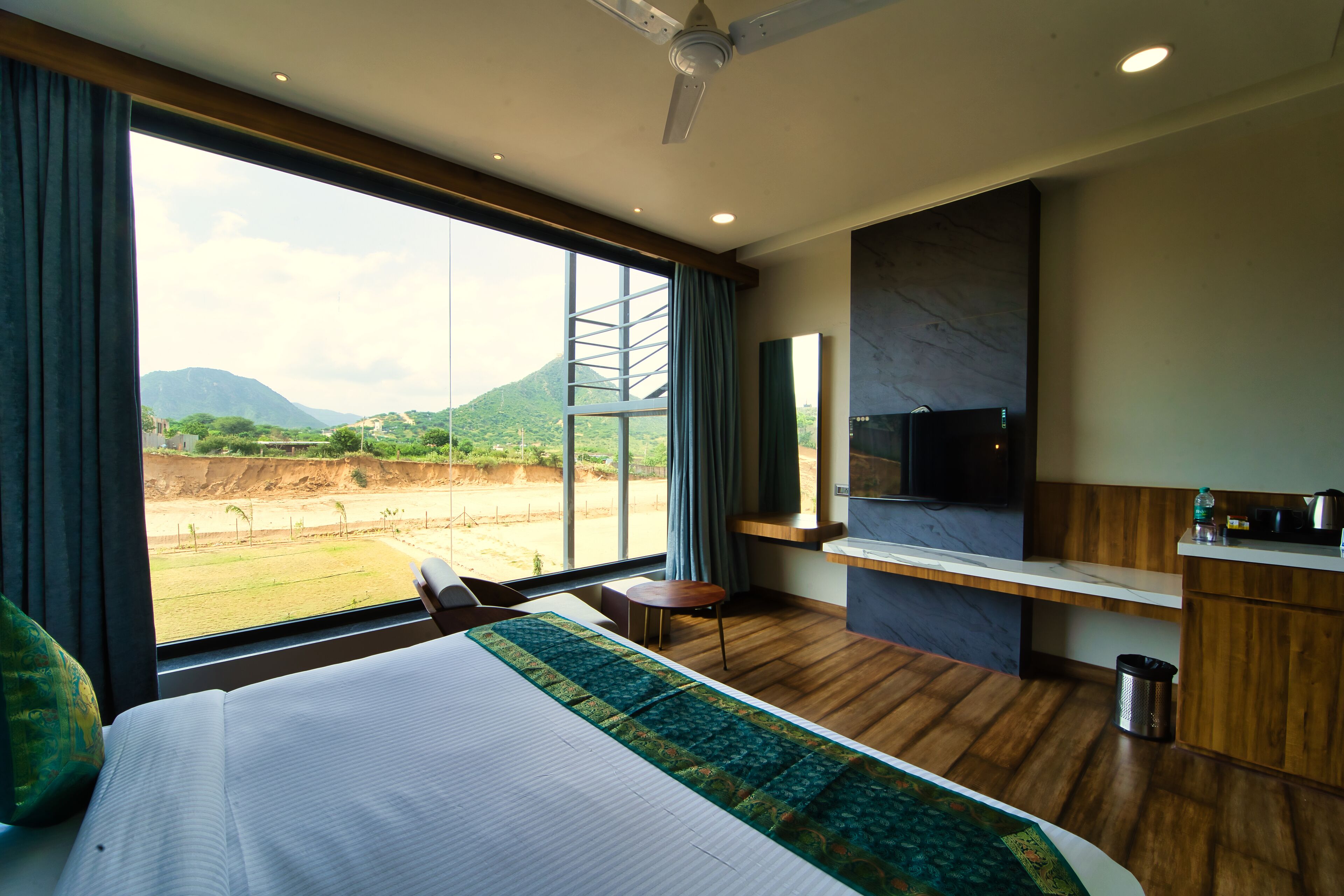 A hotel room with a large bed, a desk, a TV, and a view of a mountainous landscape.