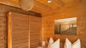 Ett sovrum i en stuga med träpanel, en stor säng, en trägarderob och en tavla som hänger på väggen och föreställer en brygga.