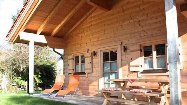 En stuga byggd av trä med en inglasad veranda, två solstolar, ett picknickbord och en liten trädgårdsdel.
