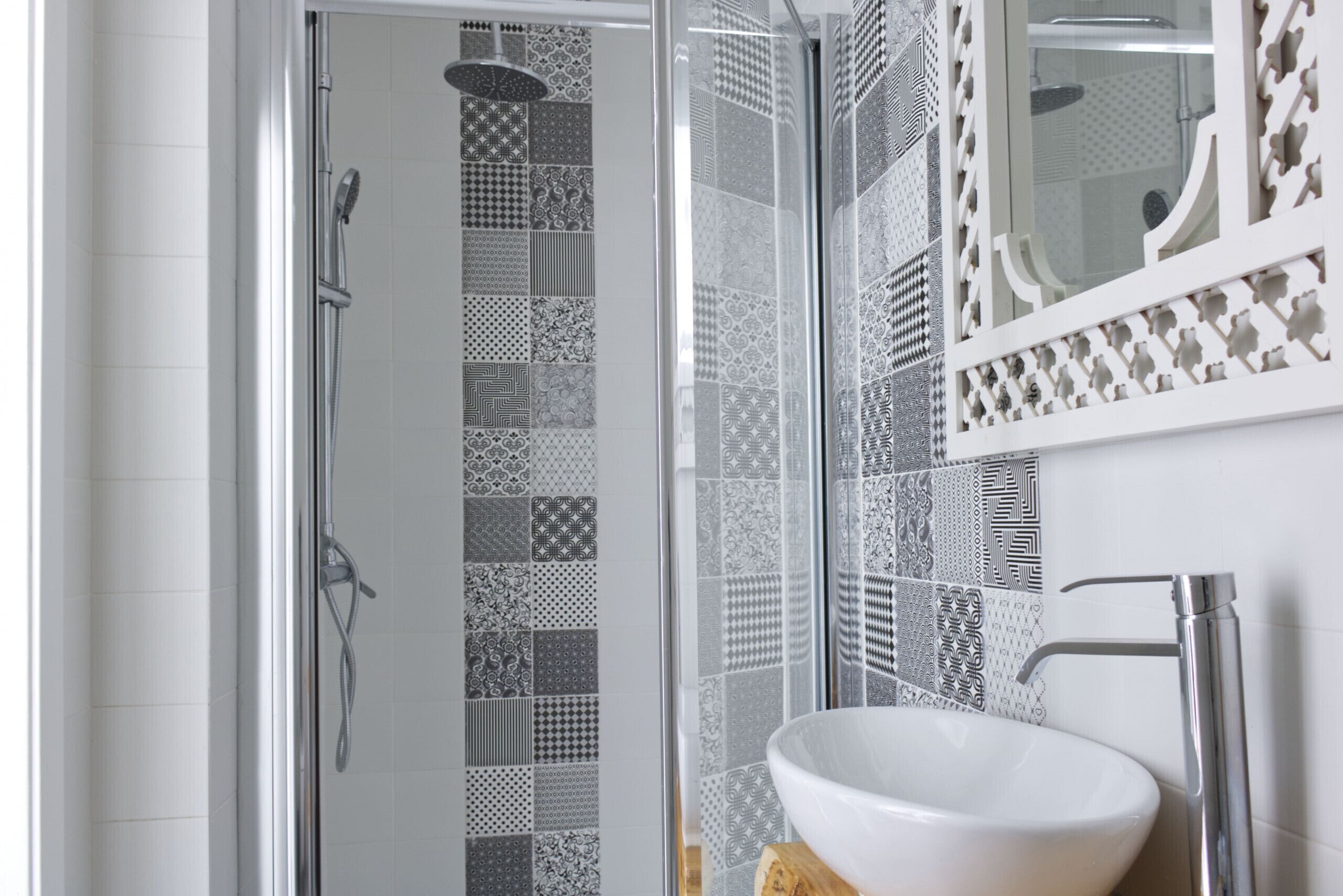 A bathroom with a glass shower enclosure, a white sink, and patterned tiles on the walls.