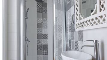 A bathroom with a glass shower enclosure, a white sink, and patterned tiles on the walls.