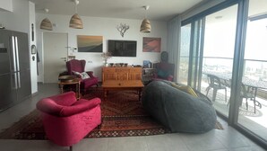 A modern living room with a large window, a kitchen area, and a dining space.