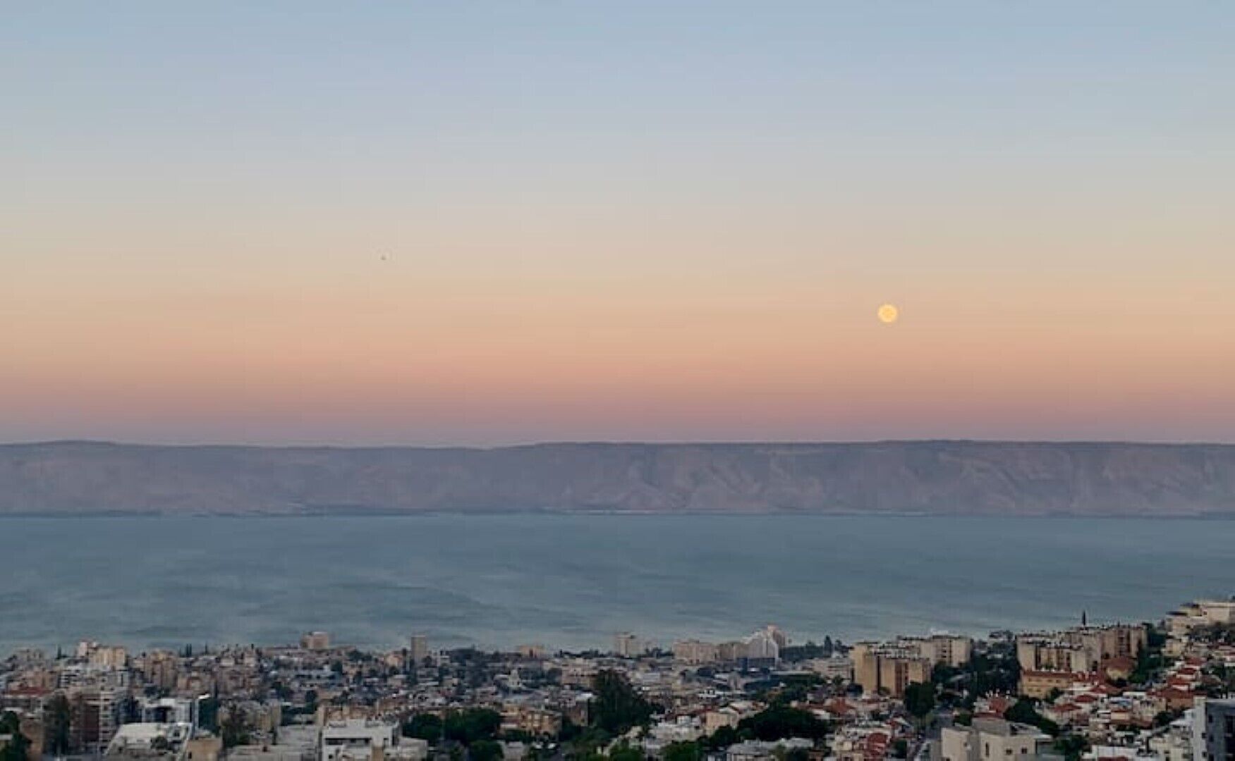 A coastal cityscape with a clear view of the sea and a distant mountain range.