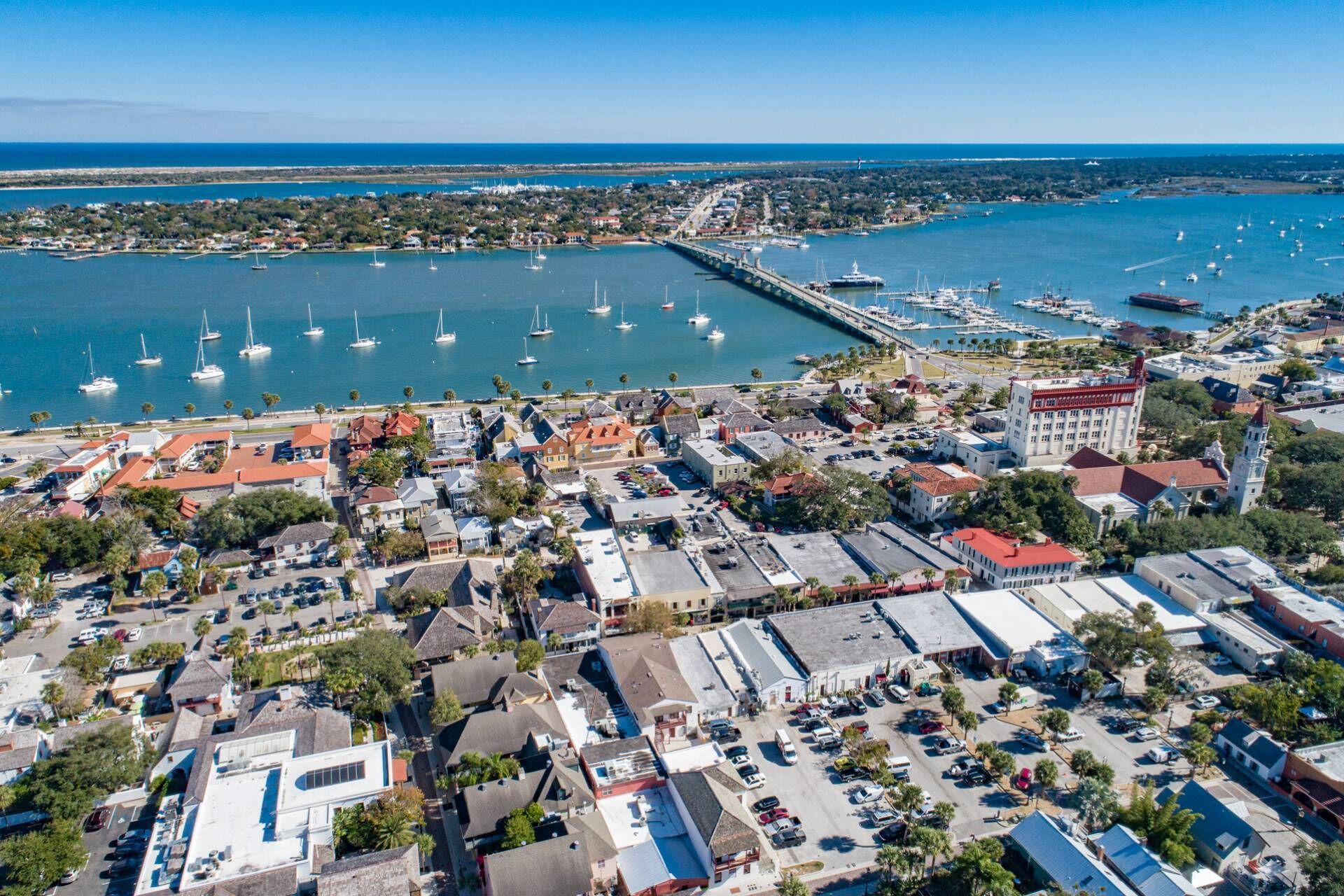 Vue aérienne d’une ville côtière avec un port de plaisance, des bâtiments et un pont reliant la ville au continent.