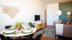 A dining area with a round table set for four, a television mounted on the wall, and a sofa in the background. - Maison Moz - Maputo View III (Maputo)