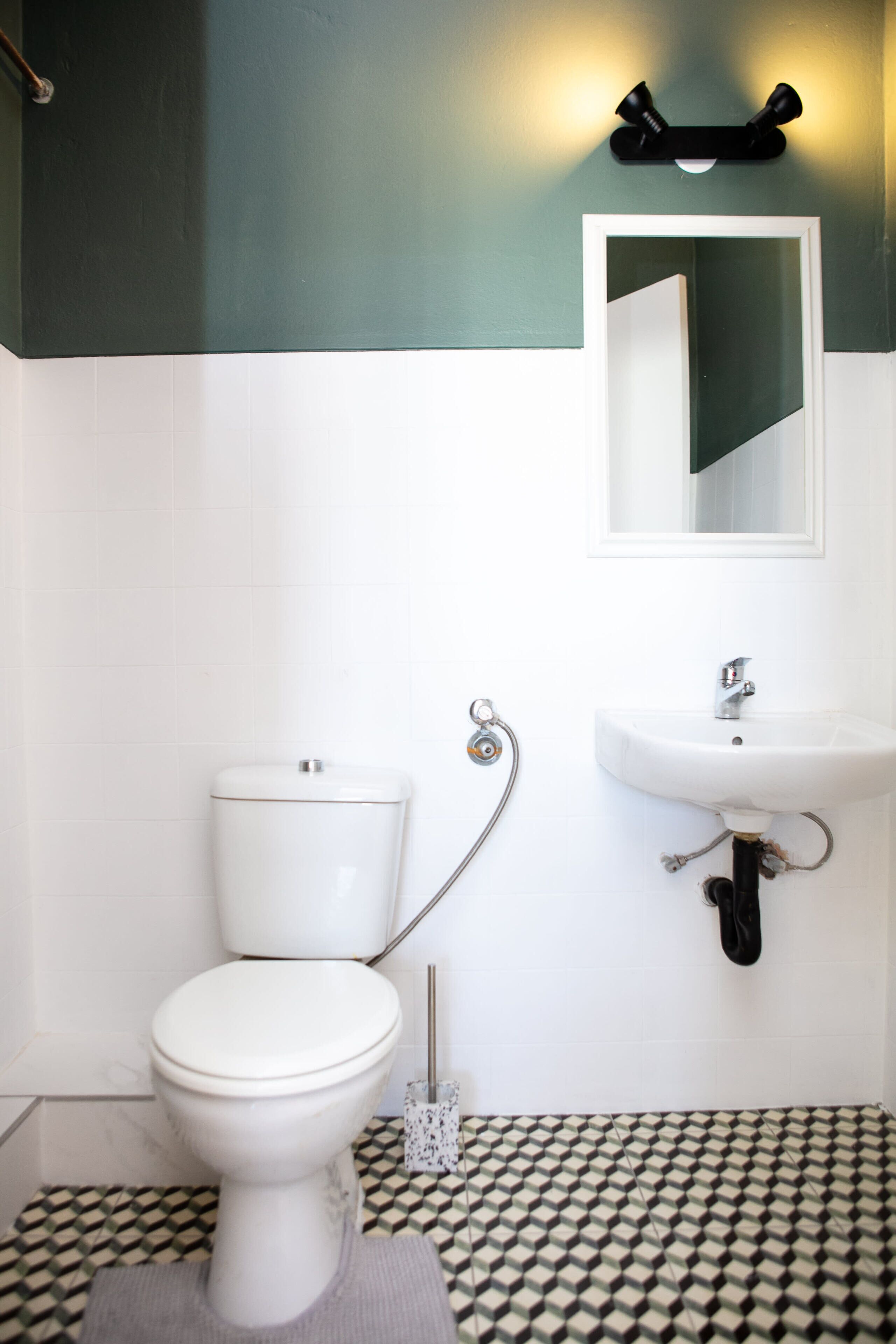 Un baño con inodoro blanco, lavamanos y espejo.
