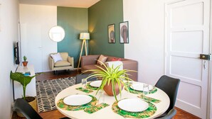 A dining area with a round table set for four, a potted plant, and a sofa in the background. - Maison Moz - Maputo View III (Maputo)