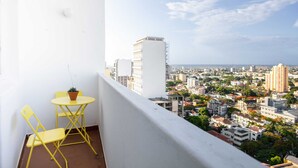 A balcony with yellow chairs and a small table, overlooking a cityscape with various buildings and a clear sky. - Maison Moz - Maputo View III (Maputo)