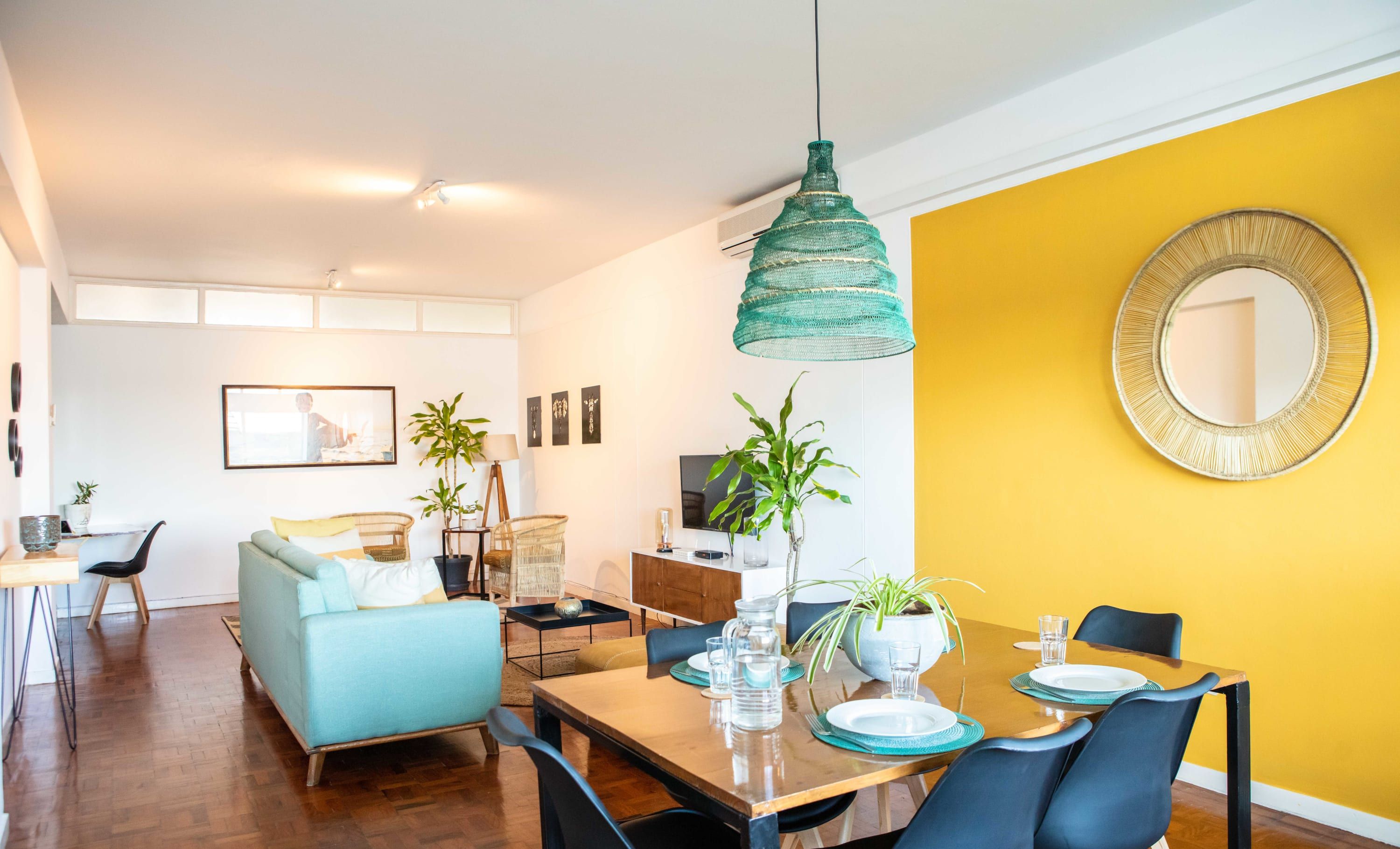 A modern living room with a dining area, featuring a sofa, dining table, chairs, and a hanging light fixture.