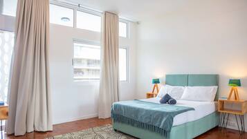 A bedroom with a bed, two bedside tables with lamps, a window with curtains, and a patterned rug.