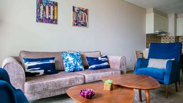 A living room with a sofa, armchair, and coffee table. There are two abstract paintings on the wall.