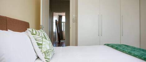 A bedroom with a bed, a wardrobe, and a hallway leading to another room.