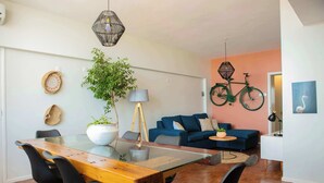 A modern living room with a glass dining table, black chairs, a blue sofa, a green bicycle, and a potted plant.