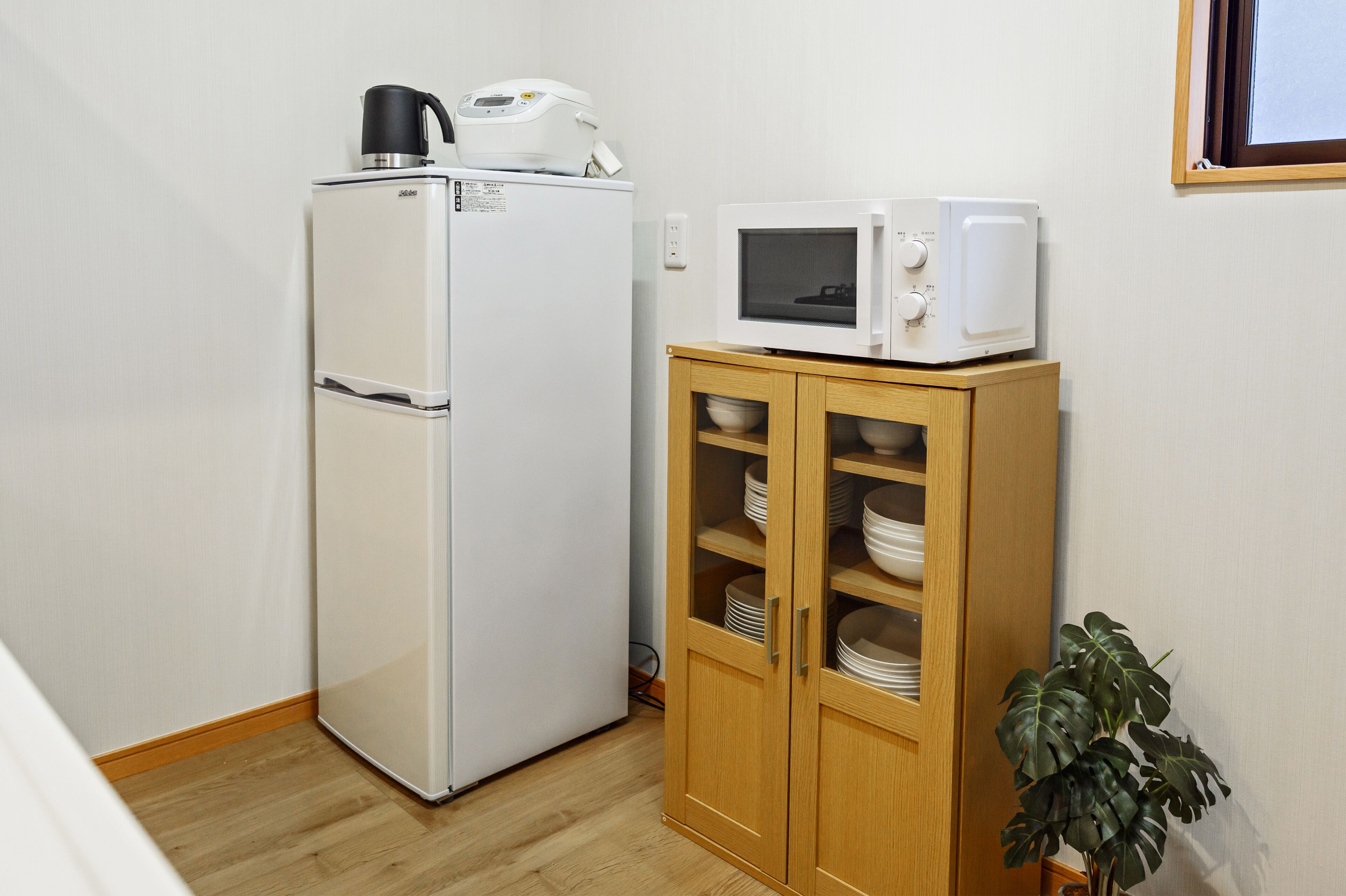 Une cuisine compacte avec un réfrigérateur blanc, un four à micro-ondes placé sur le dessus, et un meuble en bois doté d’étagères.