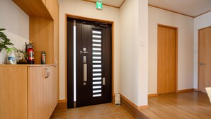 Un pasillo con una puerta de madera, un extintor y una planta pequeña sobre una estantería.