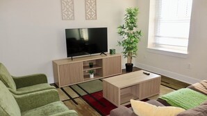 Un salon avec un téléviseur à écran plat, une plante en pot, une table basse en bois et un tapis rouge et beige.