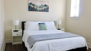 Une chambre à coucher avec un lit, des tables de chevet, une lampe, un tableau et une fenêtre.