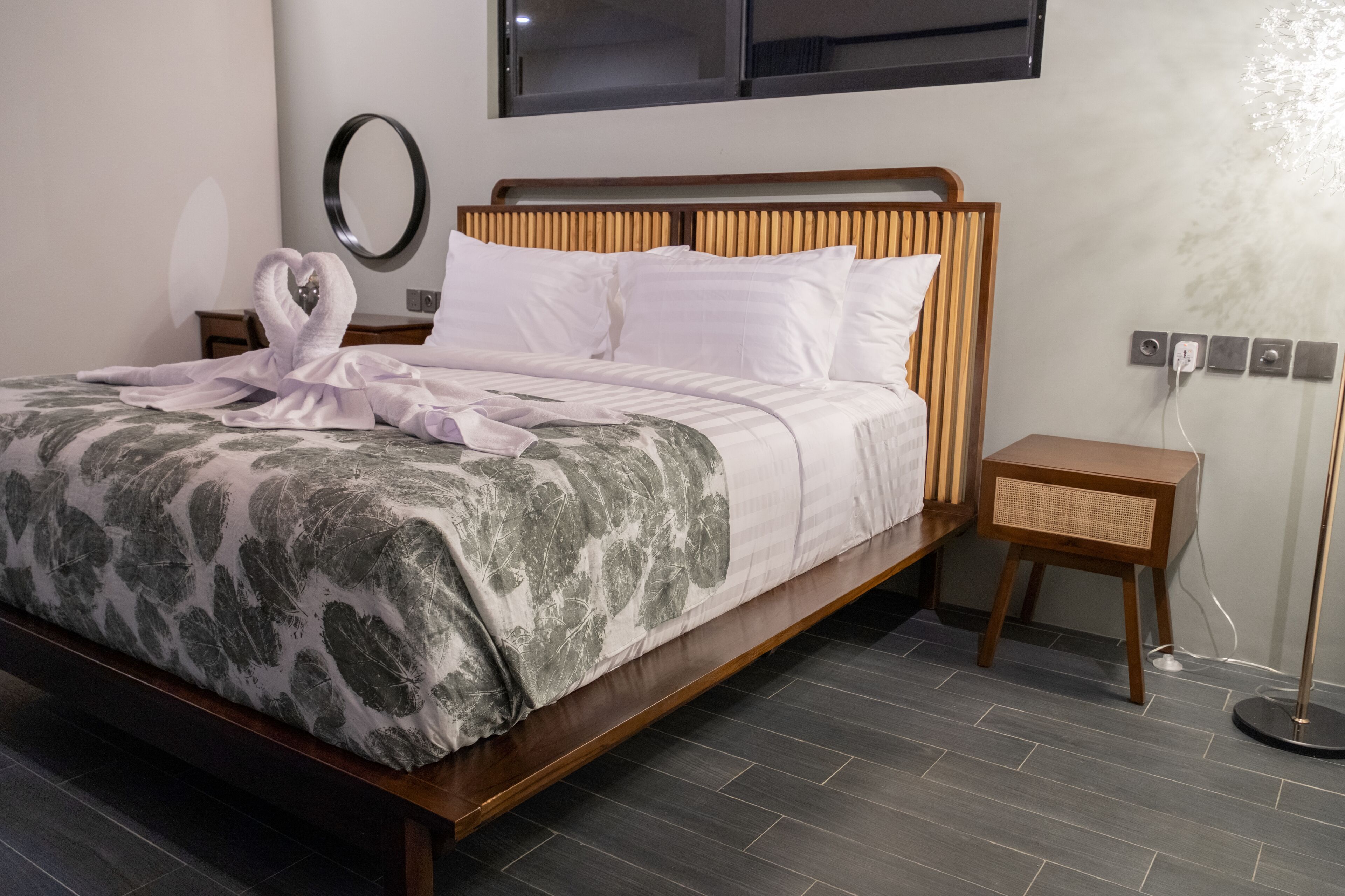 A neatly made bed with a floral bedspread, a bedside table with a lamp, and a wall-mounted mirror.