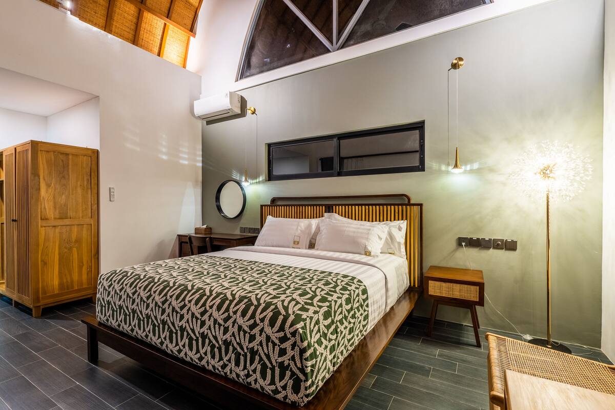 Une chambre à coucher avec un lit, une armoire en bois, des tables de chevet, une lampe et un miroir au mur.
