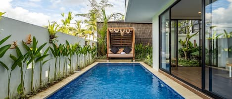 Ein moderner Poolbereich mit einem klaren, blauen Pool, einem Holz-Schaukelstuhl und üppigen tropischen Pflanzen.