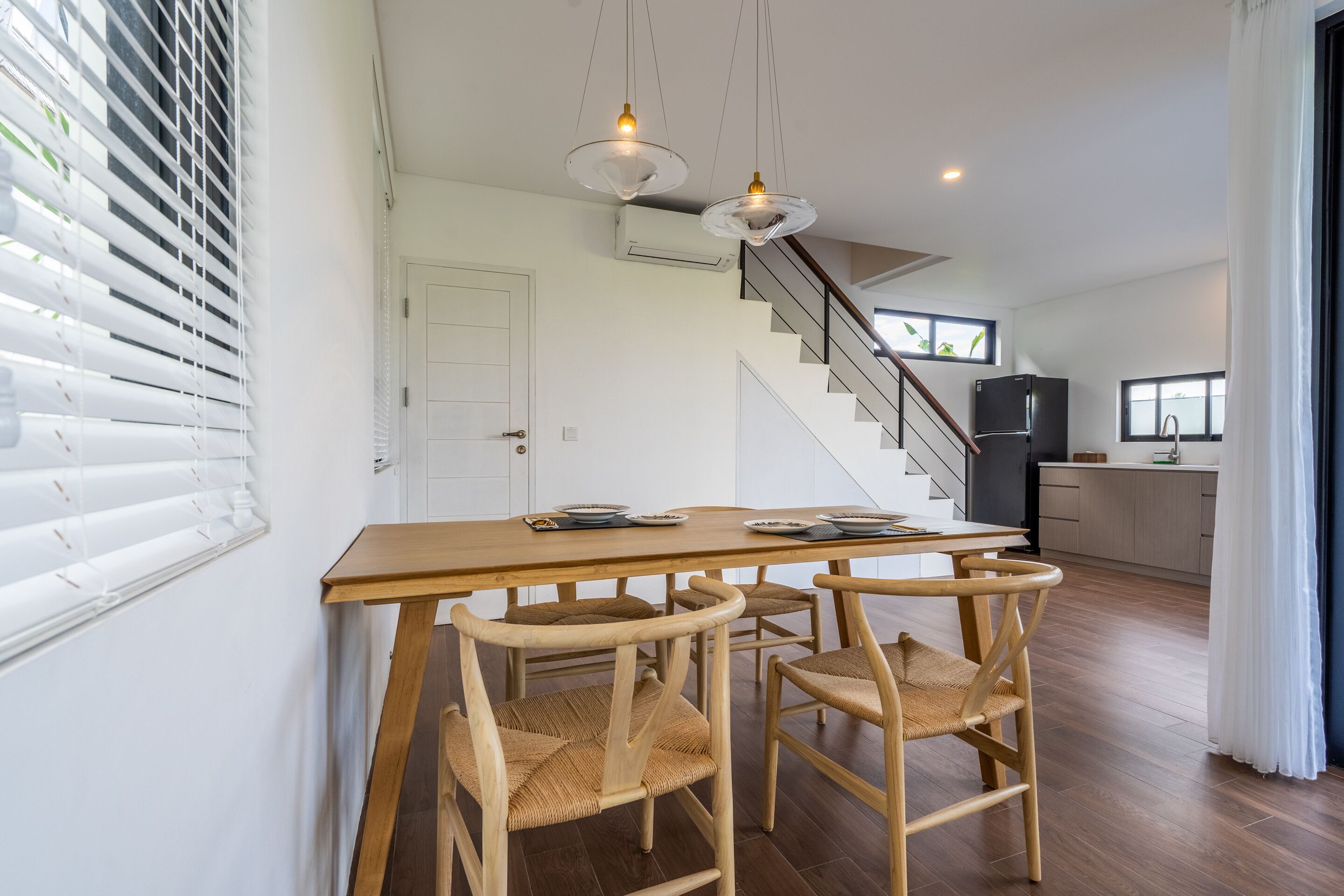 Een eetgedeelte met een houten tafel en stoelen, een trap en een keuken op de achtergrond.
