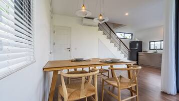 Een eetgedeelte met een houten tafel en stoelen, een trap en een keuken op de achtergrond.