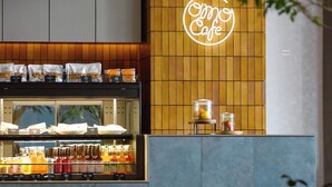 Interior de una cafetería con un letrero de neón, una exhibición de aperitivos envasados y un refrigerador de bebidas.