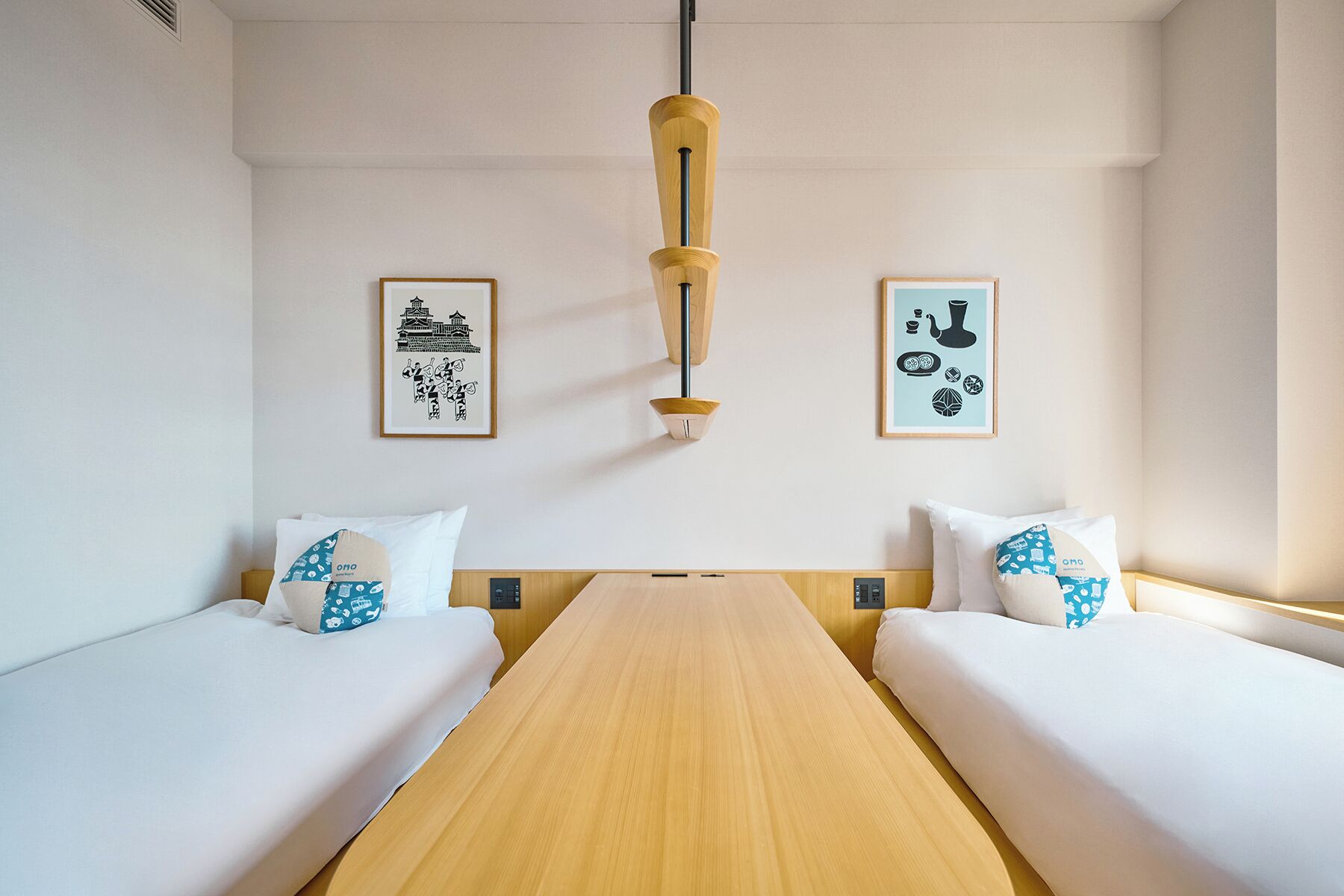 A hotel room with two single beds, a wooden table, and two wall-mounted light fixtures.