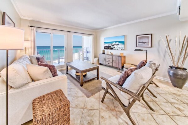 A spacious living room with a large window overlooking the sea, a sofa, a coffee table, and a decorative vase.
