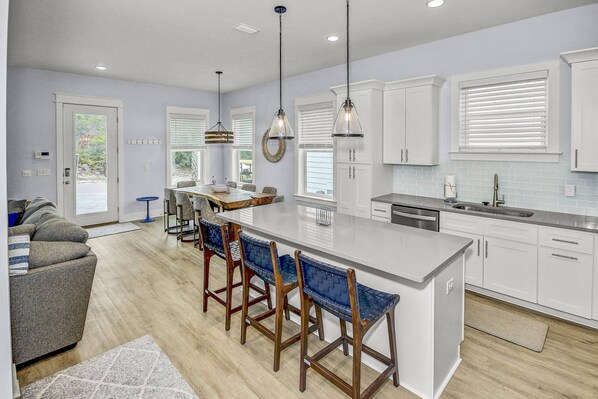A modern kitchen with white cabinets, a large island with bar stools, pendant lighting, and a view of the outdoors through the windows.