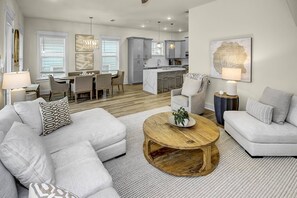 A modern living room with a grey sofa, a round wooden coffee table, and a dining area with a white table and chairs. - New 4BR Beach Home w/ Free Golf Cart, Pool View, & Balcony Near Emerald Coast, Shops and Restaurants (Santa Rosa Beach)