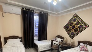 Habitación de hotel con tres camas individuales, una mesita, una silla, un adorno en la pared y un equipo de aire acondicionado.
