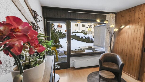 A cozy room with a large window, a potted plant, a leather chair, and a small table.