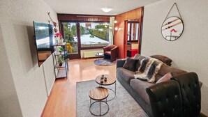 A modern living room with a sofa, two coffee tables, a TV, and a view of a snowy landscape through large windows.