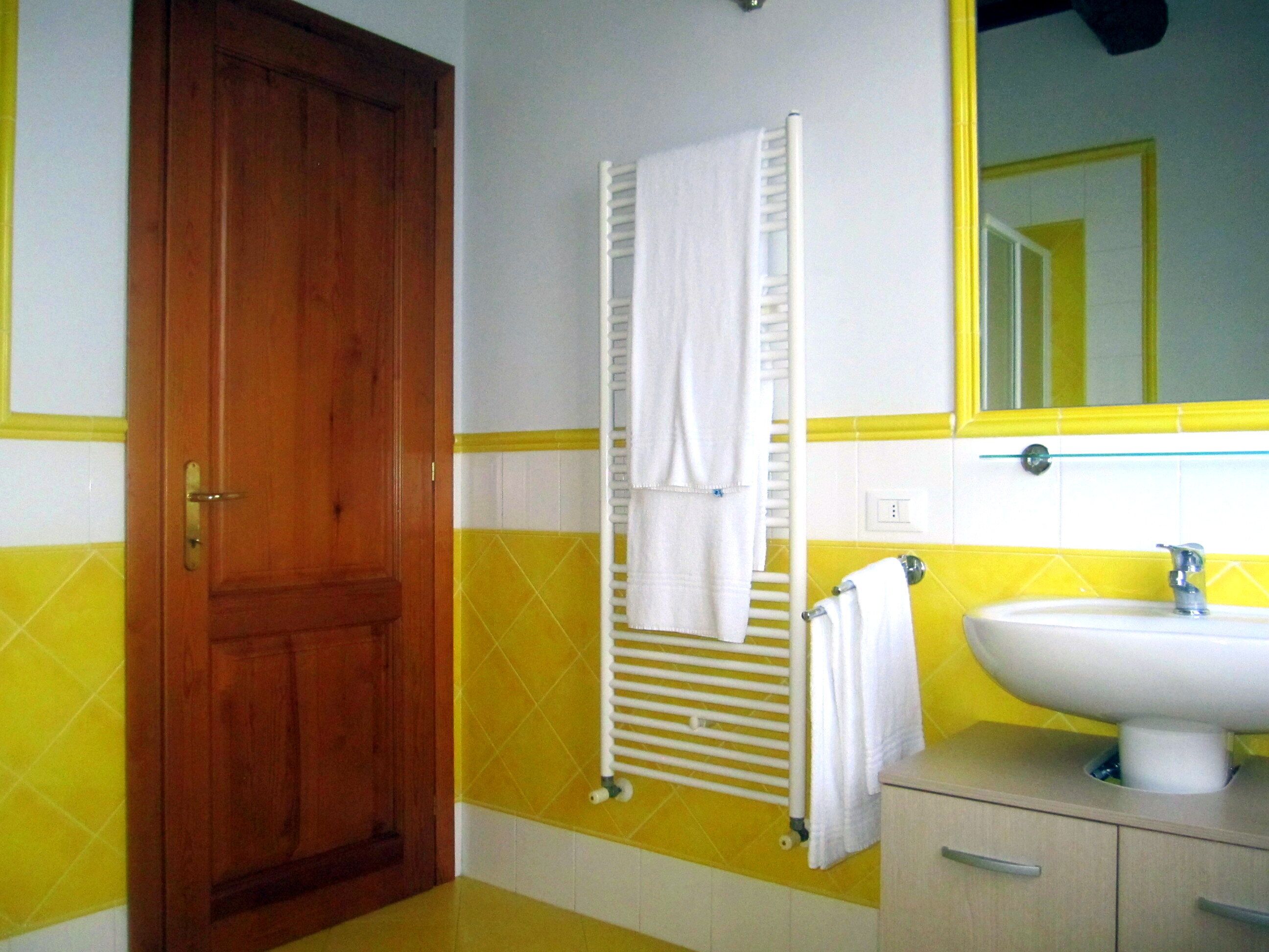 A bathroom with a wooden door, a white towel rack, a white sink, and yellow and white tiled walls.