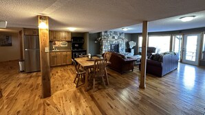 Amplia sala de estar con una mesa y sillas de comedor, una chimenea de piedra y un ventanal grande.