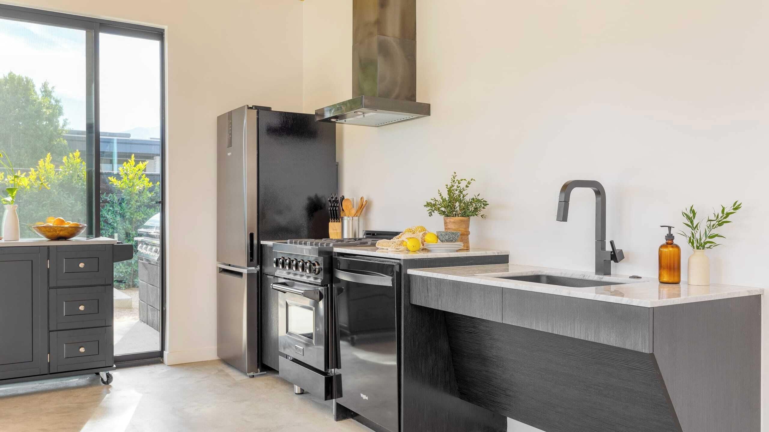 Una cocina moderna con horno empotrado, refrigerador de acero inoxidable y un amplio ventanal con vista a la vegetación.