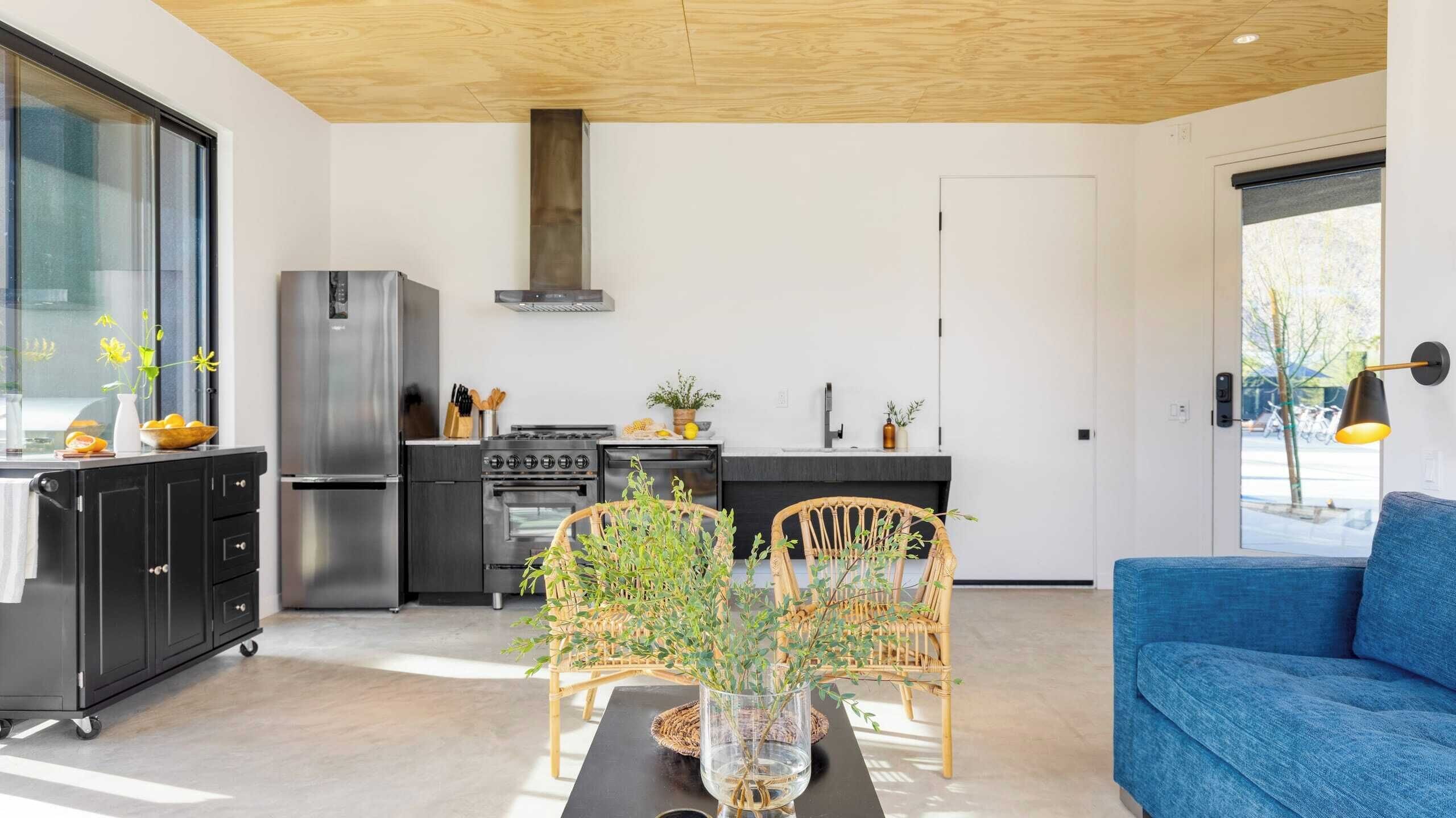 A modern kitchen with a stainless steel refrigerator, stove, and oven, a dining area with a table and chairs, and a blue sofa.