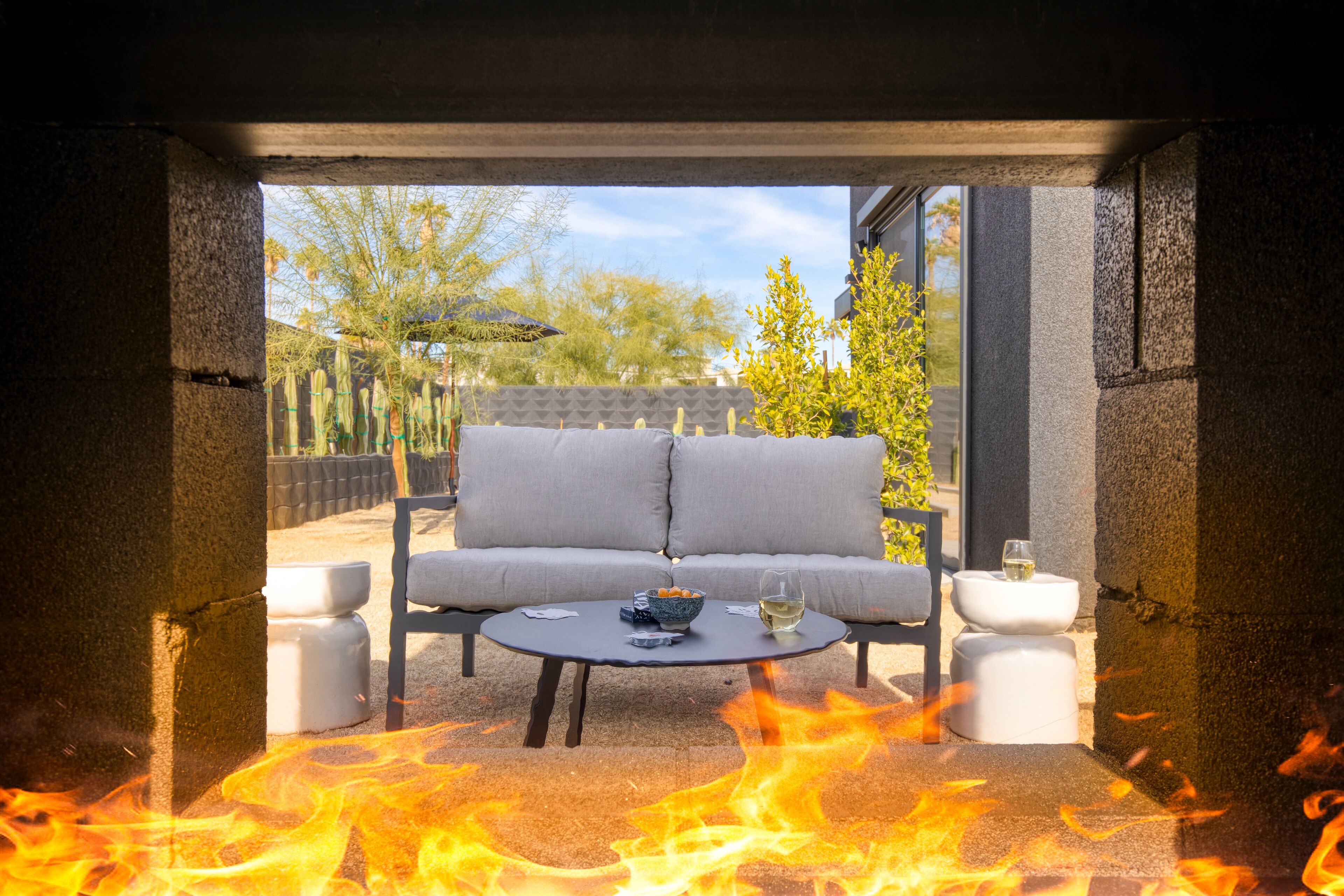 An outdoor seating area with a sofa and two white stools, a round table, and a fire feature.
