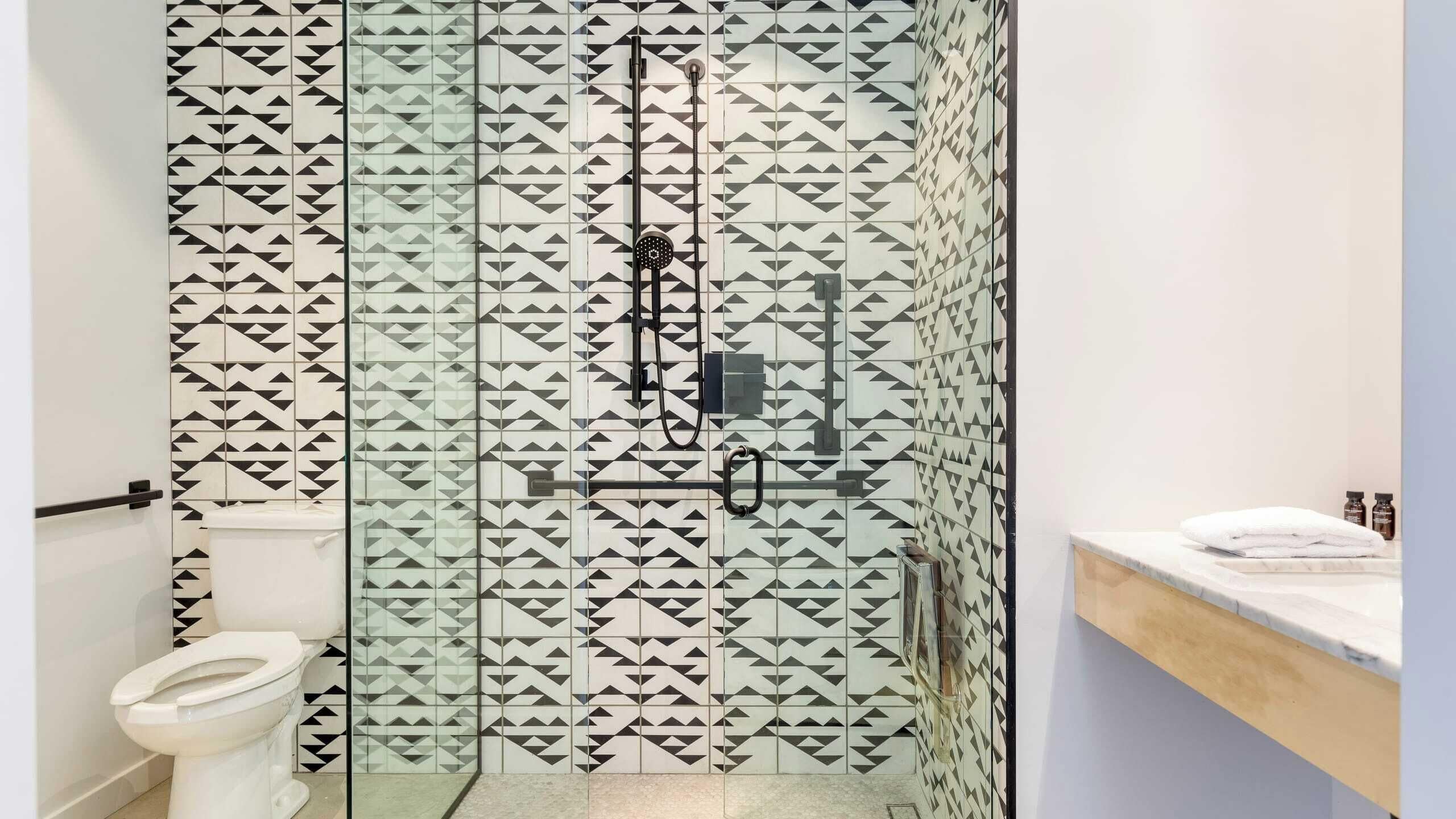 A modern bathroom with a geometric tile pattern, a glass shower enclosure, and a white toilet.
