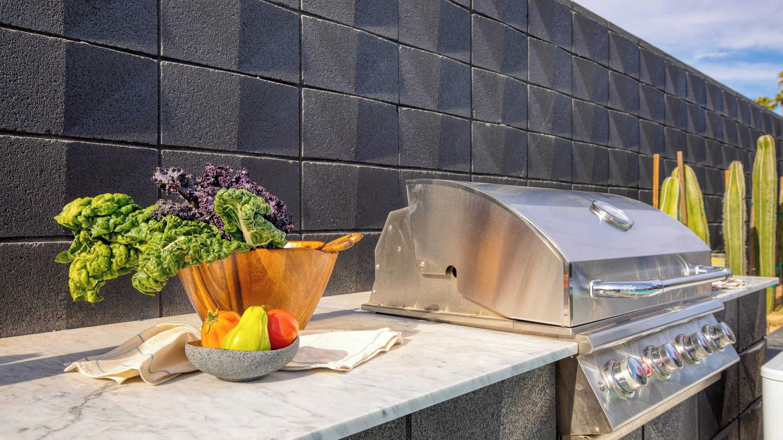 An outdoor kitchen with a grill, a bowl of vegetables, and a potted plant.
