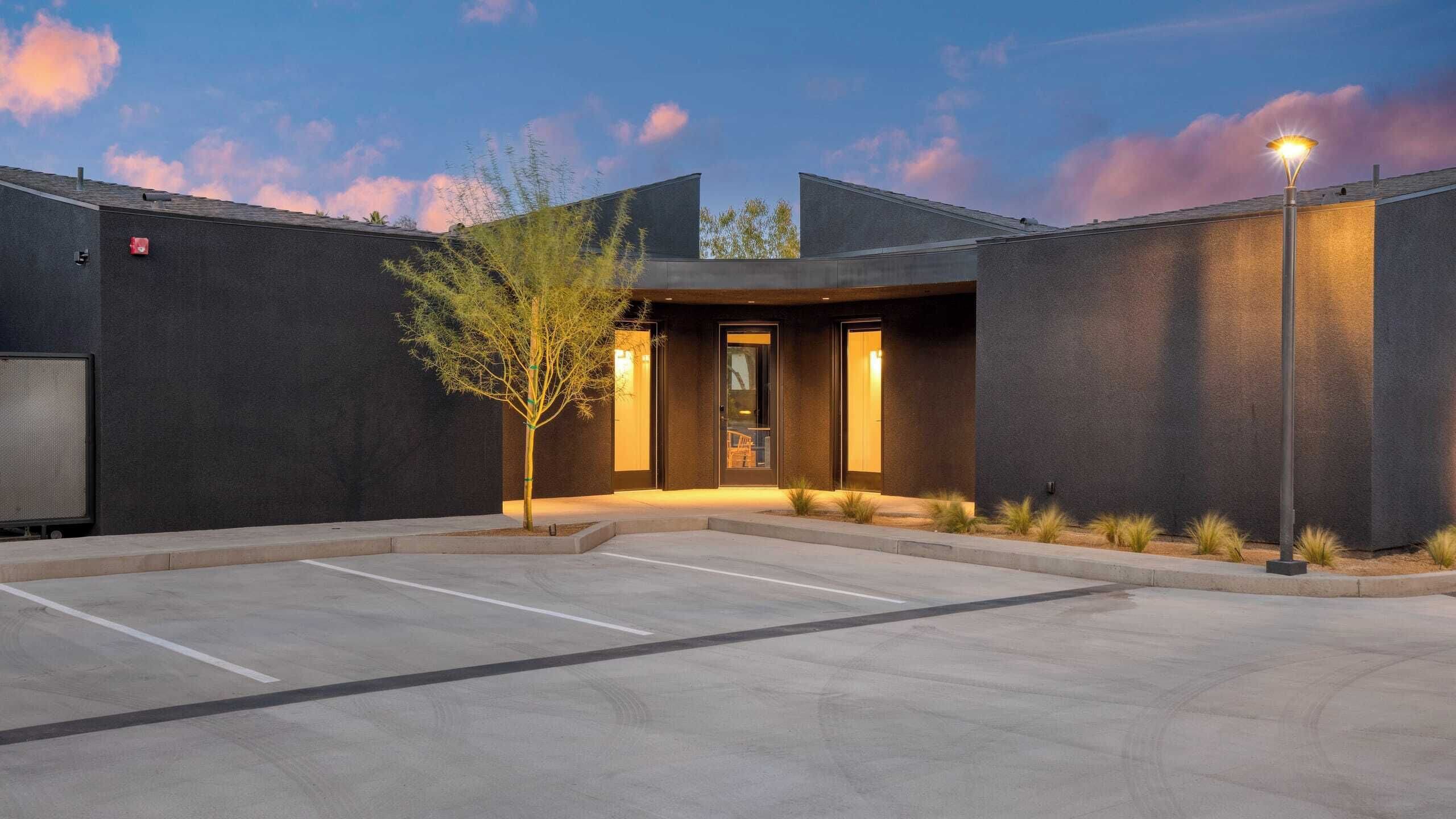 A modern building with a dark facade, a parking lot, and a street lamp.