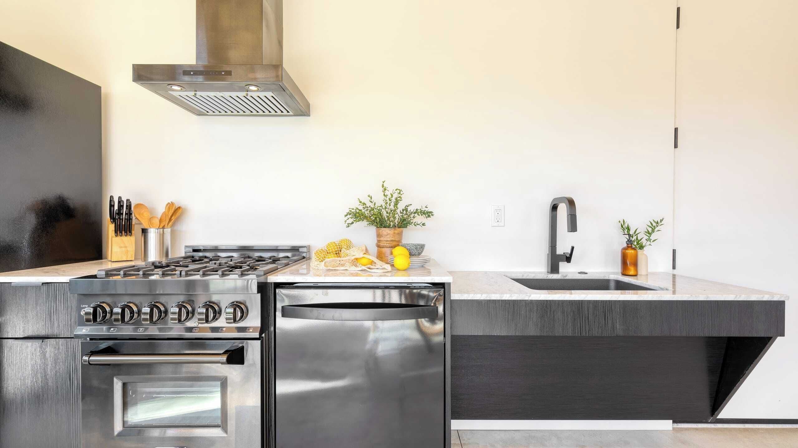 A modern kitchen with a stainless steel stove, oven, and dishwasher, a sink, and a range hood.