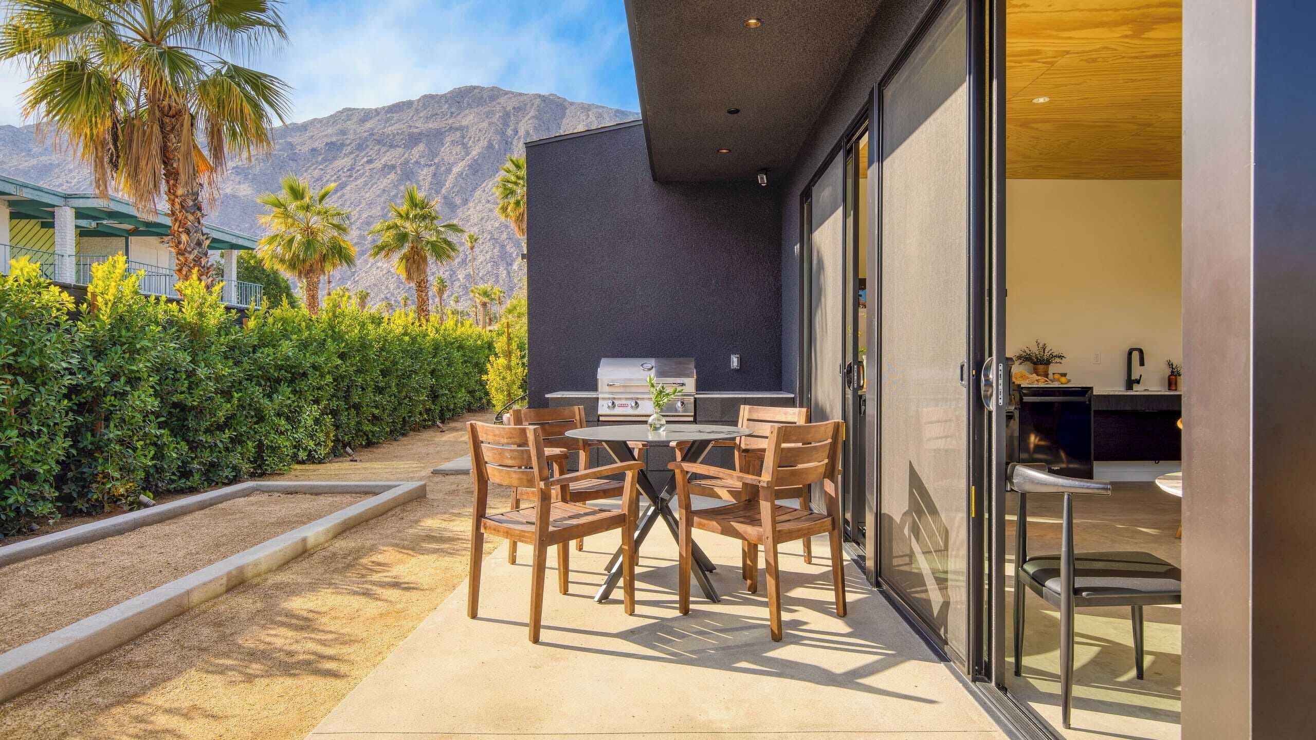 A patio with a grill, wooden chairs, and a view of mountains.